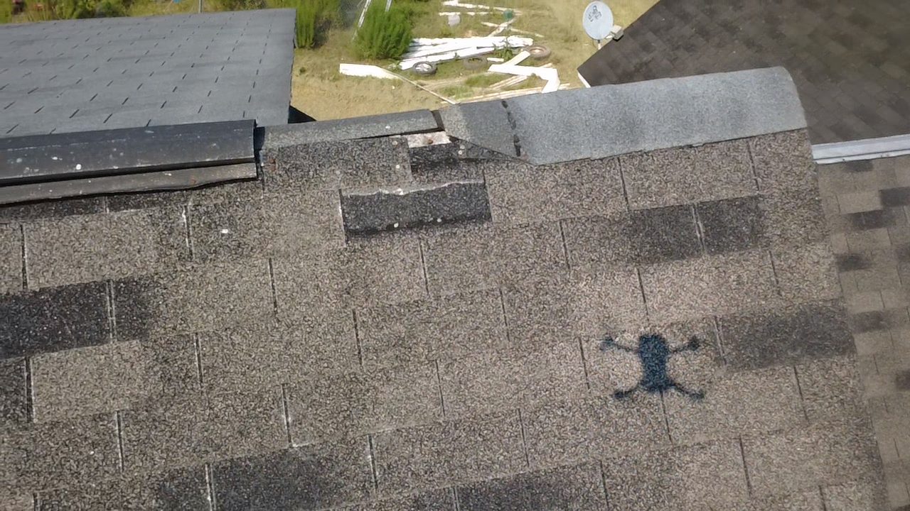 Inspection photo showing lifted and damaged shingles near the ridge